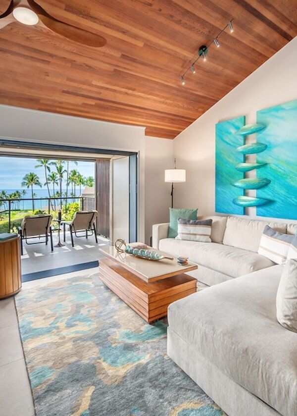 A bright, modern living room with a white sectional sofa, turquoise accents, wooden ceiling, and sliding doors opening to a balcony with ocean views.