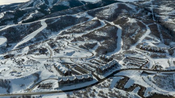 Snow-covered mountains and winding ski slopes, a village at the base with buildings along a snowy valley, tranquil alpine scenery.